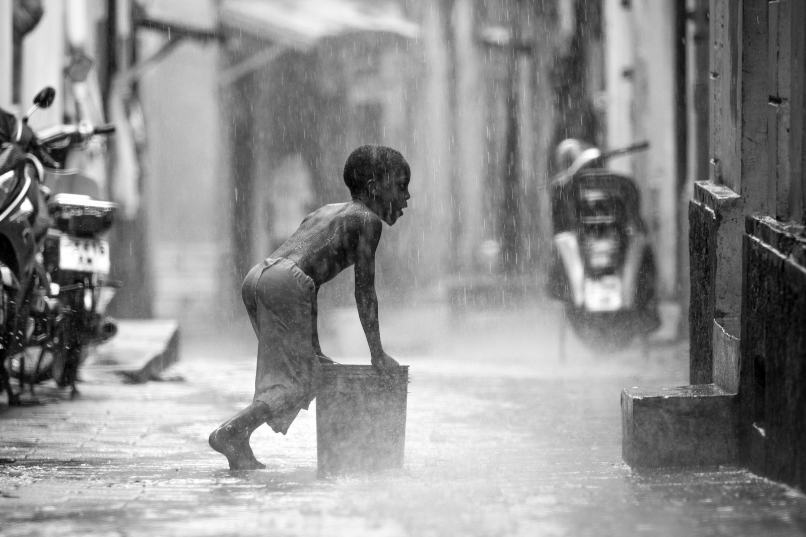 Child playing in rain on a narrow street